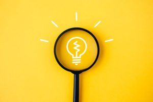 黄色い背景にある電球のマークと虫眼鏡
